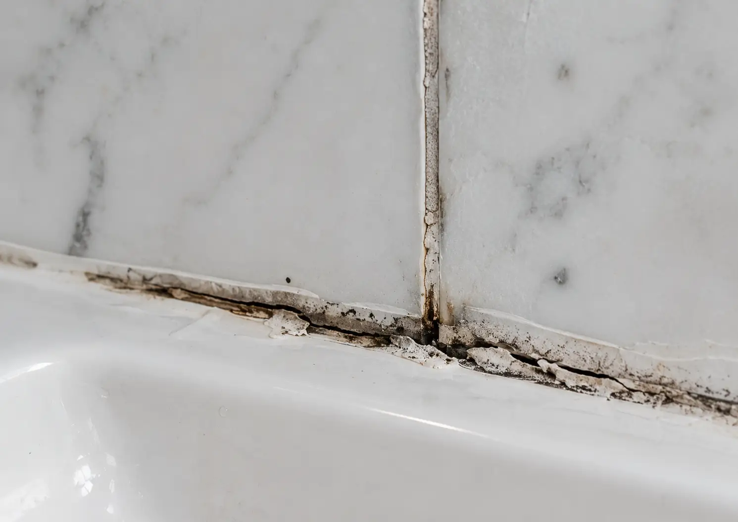 Cracked grout and perished silicone sealant at a shower tray junction