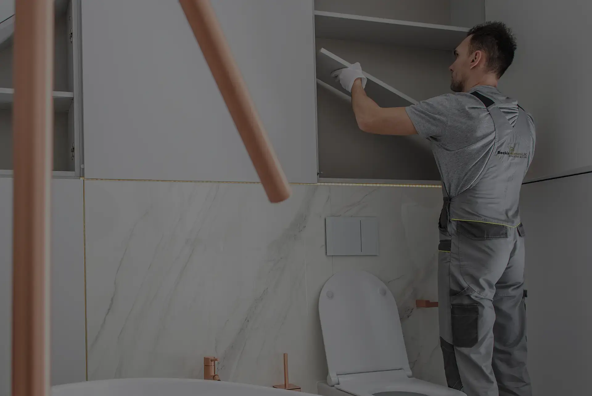 Beck's Homes UK handyman installing bathroom cabinet shelving in a modern marble bathroom
