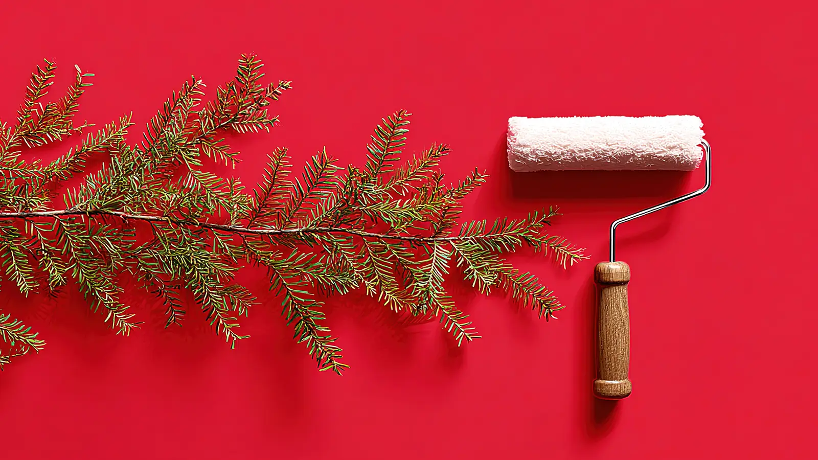 Paint roller beside a pine branch on a red wall, representing decorating before Christmas in London