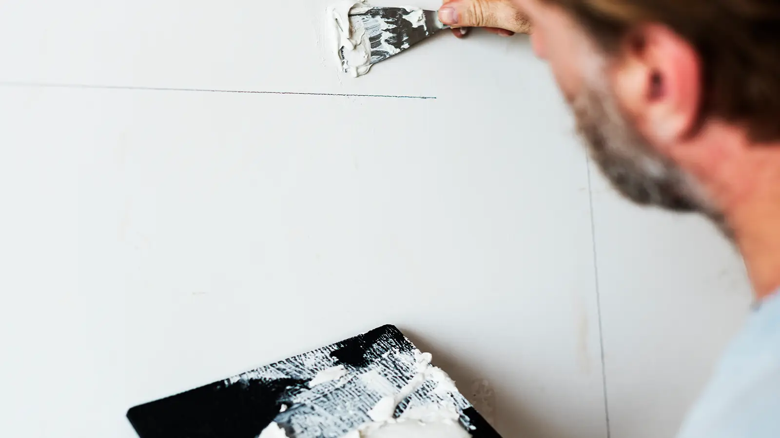 Decorator filling cracks in a plaster wall before painting a London period property